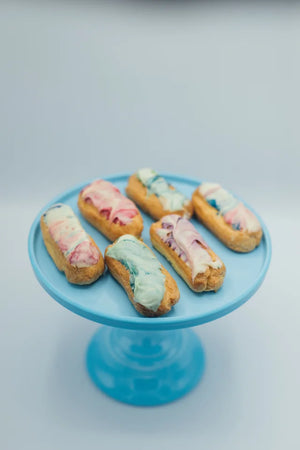 six of our rainbow eclairs sitting on a blue plate on a white background.